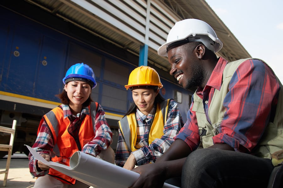 Three workers wearing safety vests and hard hats looking at a drawing